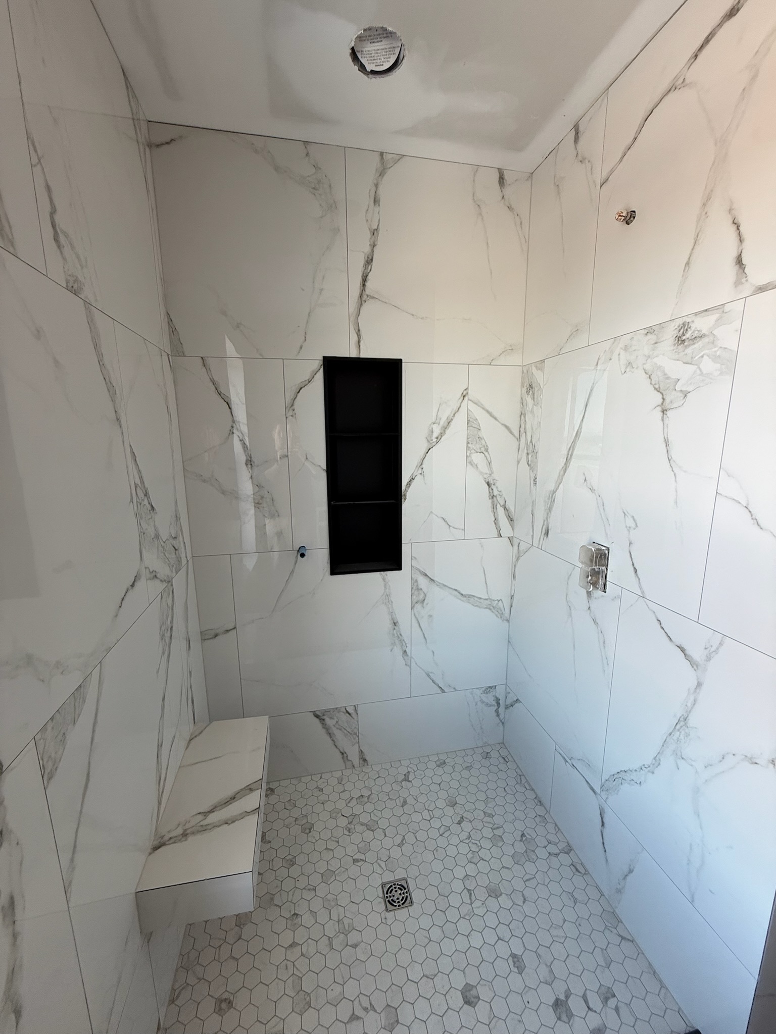 Custom calacatta tile shower with floating bench and black niche by Upstate Bath Renewal