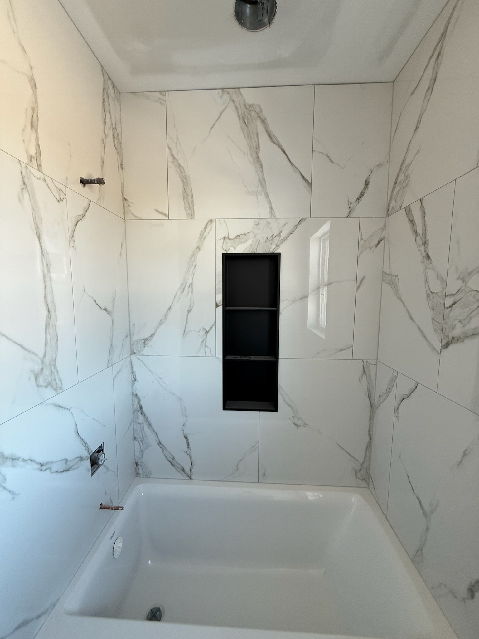 White marble-look tub surround with vertical black recessed niche in an Upstate SC guest bathroom