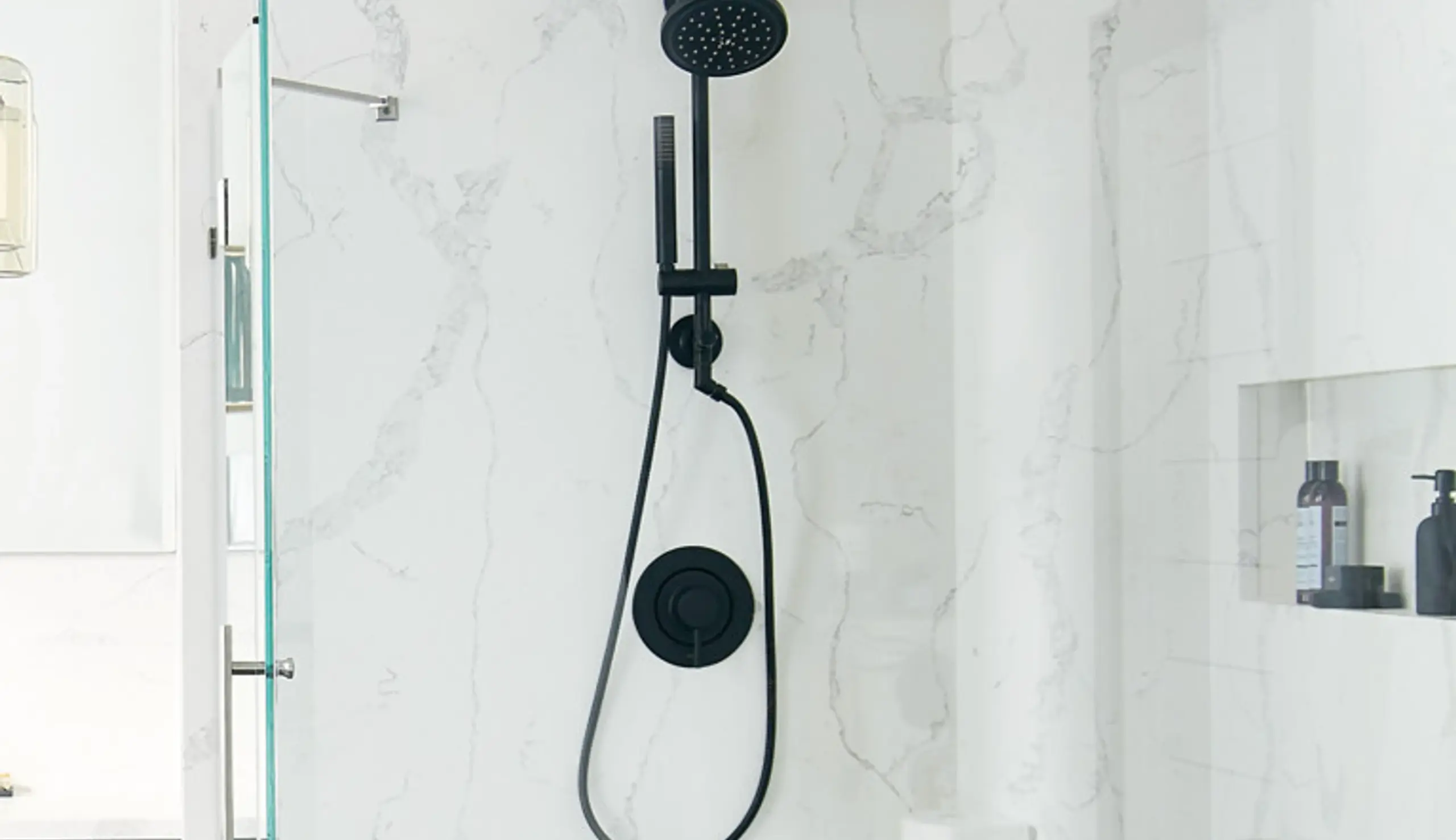 Modern black Moen showerhead and handheld sprayer mounted on a marble wall, showcasing sleek bathroom fixture design for enhanced functionality and style.