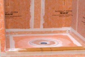 Shower base installation with Schluter waterproofing membrane, emphasizing importance of flood tests for effective bathroom waterproofing.